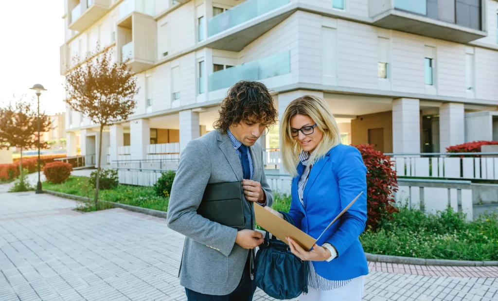 Dos profesionales consultando una carpeta frente a un edificio residencial