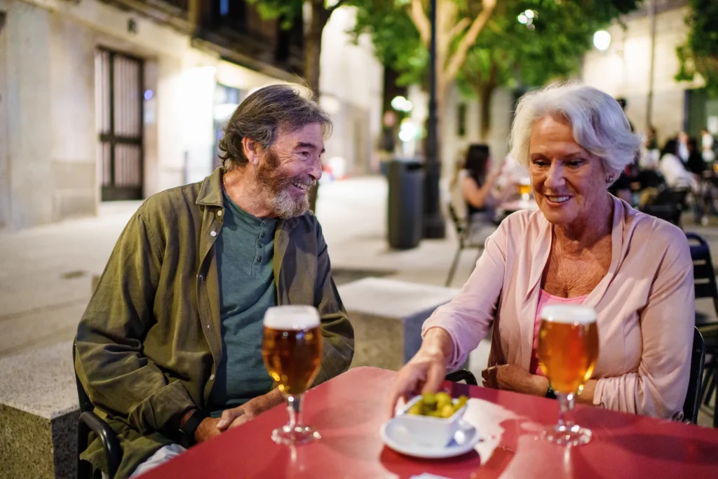 Pareja de personas mayores tomando cerveza en una terraza al anochecer