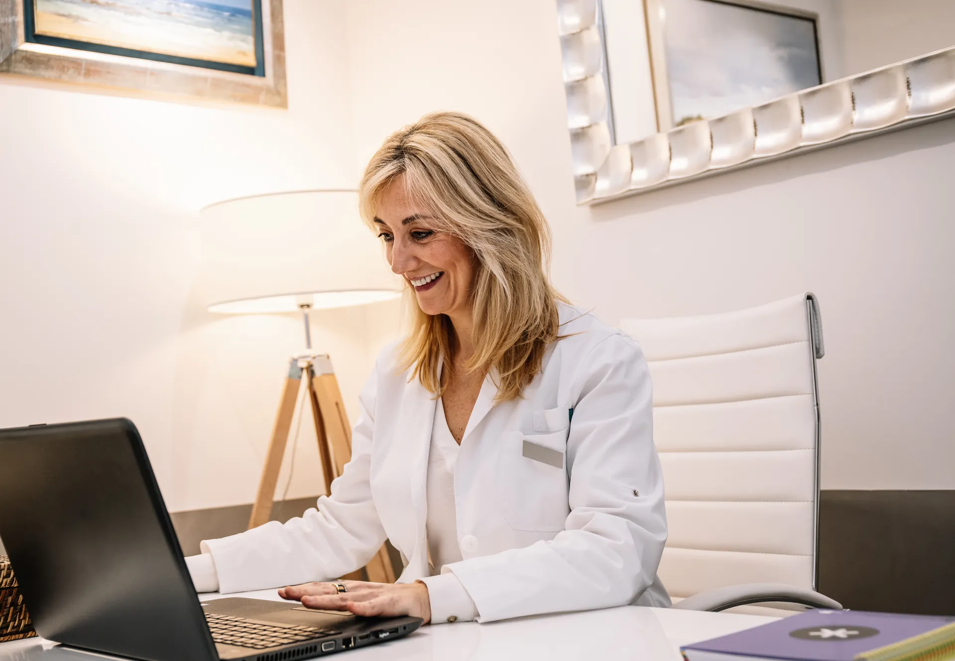 Doctora sonriente trabajando con su portátil en la mesa de la consulta