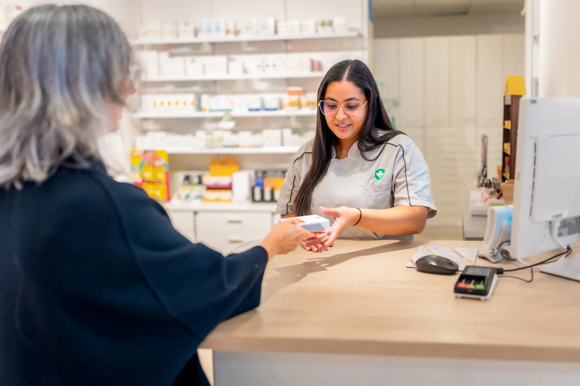 Farmacéutica entregando un medicamento a una clienta en el mostrador